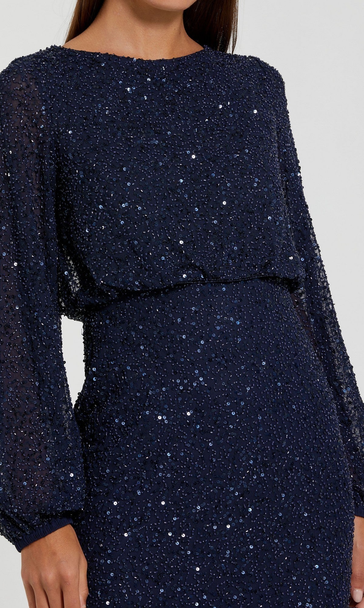 A woman wearing the Mac Duggal 94203 long formal dress, a navy blue sequin gown with long sleeves, textured fabric, and a fitted waist, stands against a plain light background. This modest dress perfectly combines elegance and sophistication.